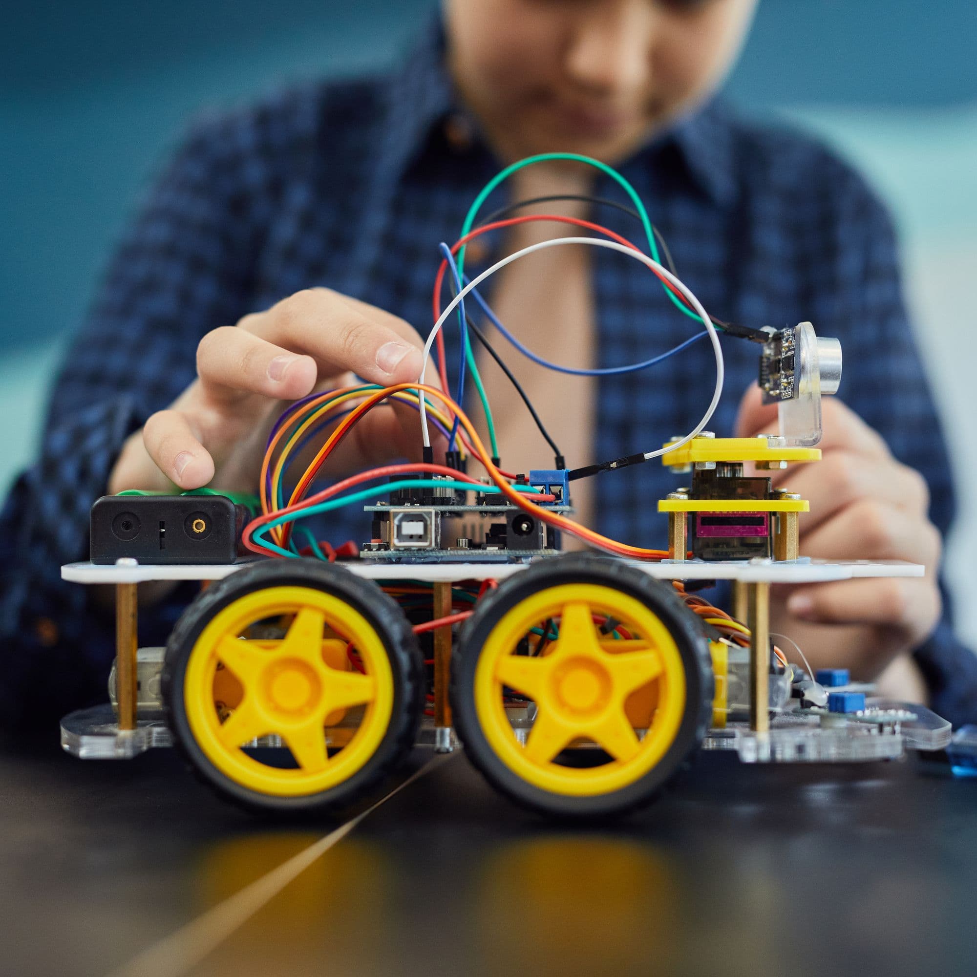 A young person wiring up a robot at a classroom desk