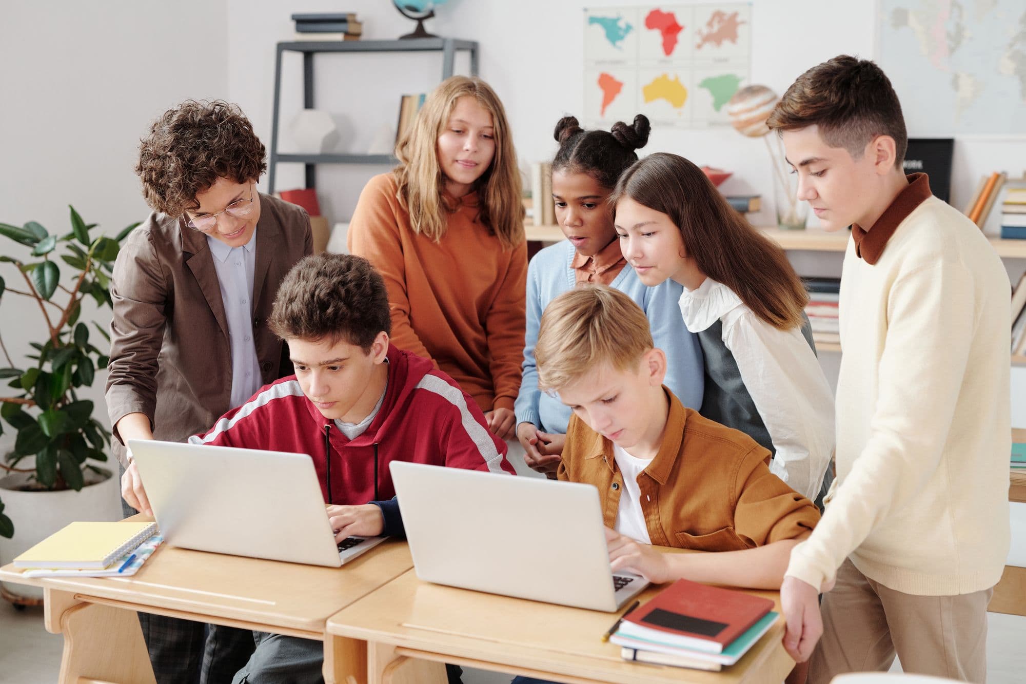 A mentor helping students on laptops in a bright classroom
