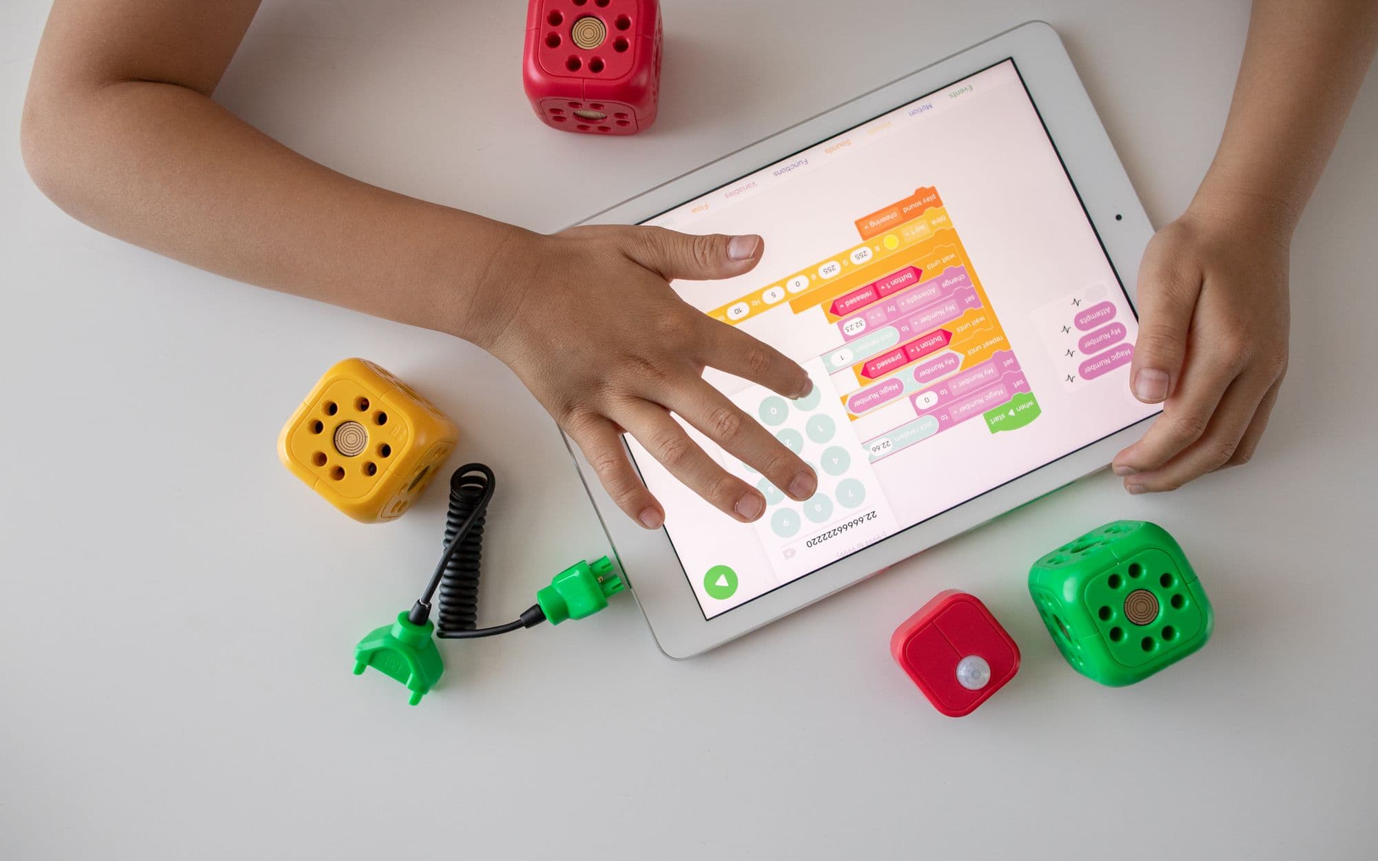 A child's hands building block-code on a tablet surrounded by coding robots